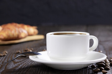 A cup of hot coffee and croissants on a black background. Breakfast with coffee and fresh pastry. Coffee beans on a table. Fresh cake and pastry