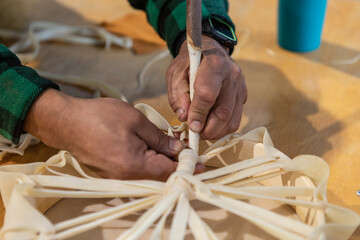Close up of man's hands tying the loose ends of a piece of leather around a wooden support to create a tambourine. Moments from a native drum workshop