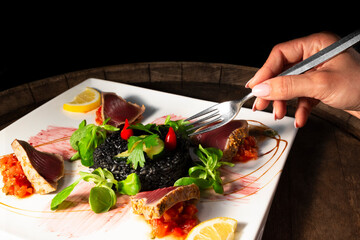 Woman hand with fork with plate of grilled tuna slices and black rice