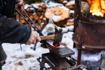 Close up shot of a hammer flattening a red, sizzling hot rod of iron out of the forge in the...