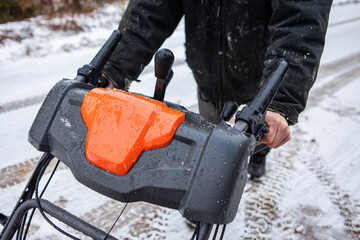 Close up shot of two male hands without gloves holding the handlebar of a bright orange snowplough. Snowplowing activity in a cold winter day. 