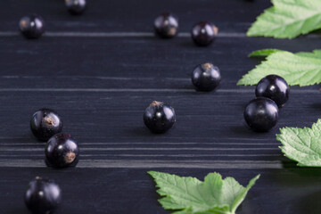 Black currant and green leaves on a dark wooden background. Background with currant berries and green leaves. Currant Macro.