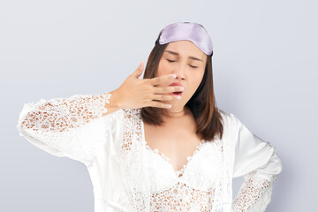 Asian woman wearing a lace white nightgown and satin robe yawning showing a sleepy gesture covering mouth with his hand.