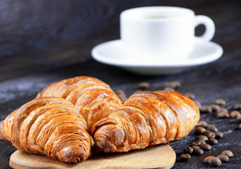 A cup of hot coffee and croissants on a black background. Breakfast with coffee and fresh pastry. Coffee beans on a table. Fresh cake and pastry
