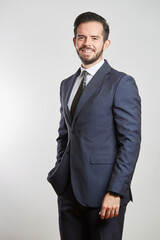 Fototapeta premium A smiling young Latino businessman standing in a dark gray suit and tie on a white background