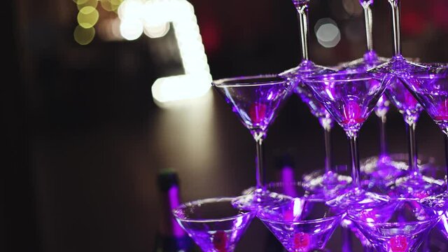 Glasses with alcoholic beverages in the pyramid, filling and pouring beautiful pyramid line of different colored alcohol cocktails with champagne on a party, catering banquet table 