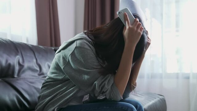 Asian woman holding the bill and smartphone in the living room and stressed by excessive expenses.