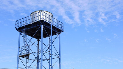 Metal water tank on the tower. Structure and storage tanks in the water supply system on a blue sky background with a copy area. Selective focus