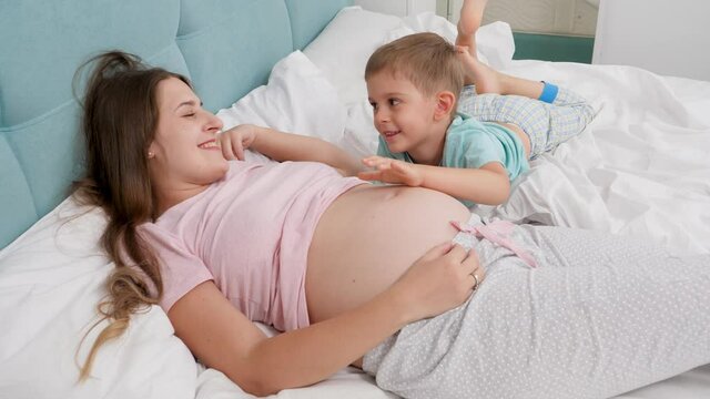 Happy smiling pregnant woman with little boy in pajamas lyin in bed and talking. Concept of loving children and family happiness expecting baby