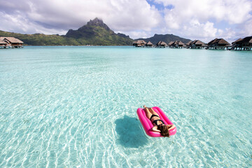 Woman floats on a pink inflatable mattress over beautiful clear, turquoise, tropical island ocean...