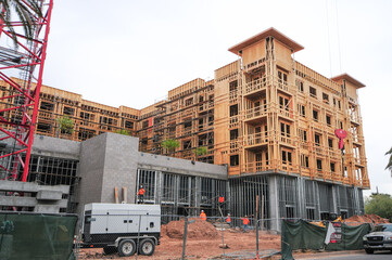 A low, angled view of an apartment complex under construction and workers installing structural...