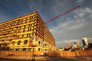 Multi-story building under construction with scaffolding and yellow sheathing, adjacent to high-rise downtown skyline and red crane, representing commercial real estate development phase © Eduardo Barraza