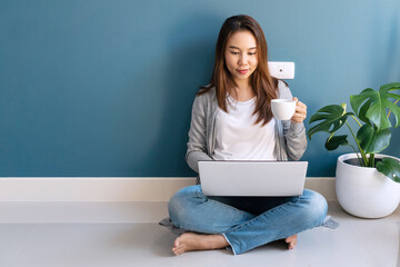 Happy young Asian businesswoman sitting on the floor using computer laptop at home. Work from/at...
