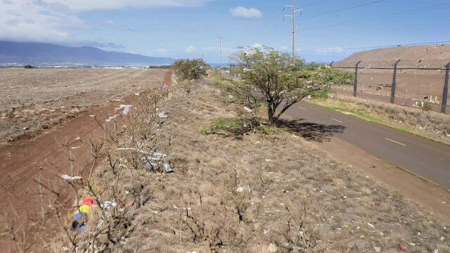 Dramatic aerial panorama of field covered by the shopping plastic bags and human waste. Strong wind blowing the garbage by the dry field with mountains on background, Hawaii, Maui island, USA 4K