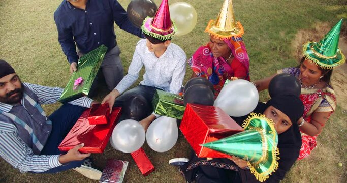 Slow-motion of mixed age group of adults, males and females, celebrating joyous enjoying with balloons, wrapped gifts and take selfie on mobile phones outdoors in summer, looking. atcamera pov