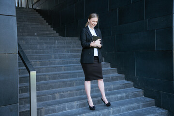 Business woman in on the steps with a notebook in her hand