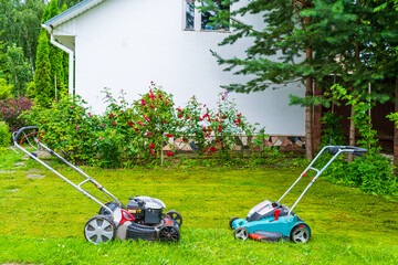 Gasoline and battery-powered lawn mowers opposite each other in a garden with flowers