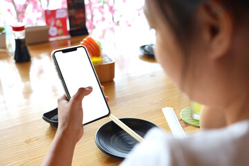 Asian woman using a smartphone in a restaurant with clipping path. A woman holding a phone with a white screen.