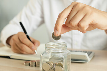Close up hand of young asian businessman,male puts a coin into the jar to calculate and financial...