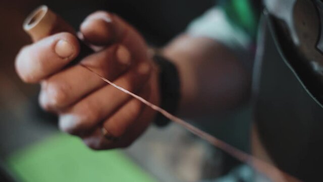 Close-up of male hands unwinding a brown spool of thread in his own workshop