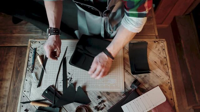 Top view of a craftsman creating a black leather wallet on wooden table