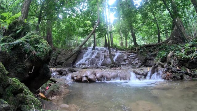 waterfall in green forest lush trees with daylight shine thought trees leaves, clean and clear water smoothly fall down in many different level. travel in summer holiday season concept