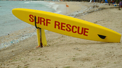 Yellow surfboard on beach with red text surf rescue emergency on a beach