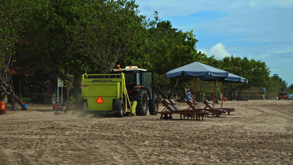 Obraz na płótnie Canvas Tractor technic for cleaning the sea beach from garbage stands on the sand after throwing plastic garbage from the sea on the island of Bali
