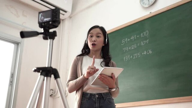 Asian woman teacher standing online teaching with headphone and digital tablet	
