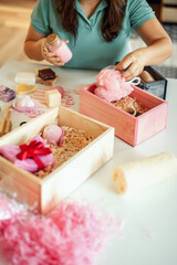 Woman preparing pink colored heart shaped gift boxes with organic natural cosmetics of body care