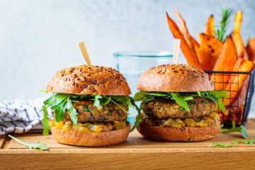 Vegan lentil burger with arugula, mustard sauce, fresh vegetables and sweet potato fries on wooden...