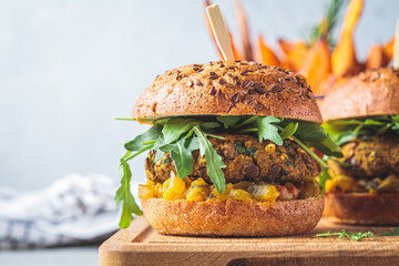 Vegan lentil burger with arugula, mustard sauce, fresh vegetables and sweet potato fries on wooden...