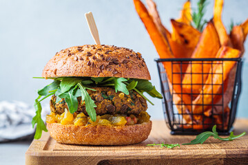 Vegan lentil burger with arugula, mustard sauce, fresh vegetables and sweet potato fries on wooden board. Vegan food concept.