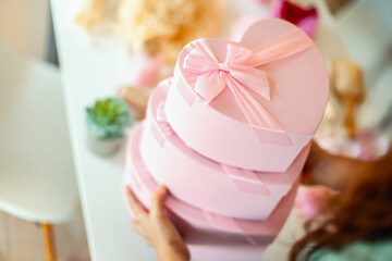 Woman hands holding pink colored heart shaped gift boxes of bath and body products for bridesmaids.