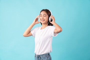 Young Asian woman standing on a blue background and hand touches on white headphones.