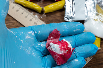 evidence of smuggling traffic: Packaging of a narcotic substance in the hand of a forensic expert against the background of other arrested materials, cocaine, heroin, spice