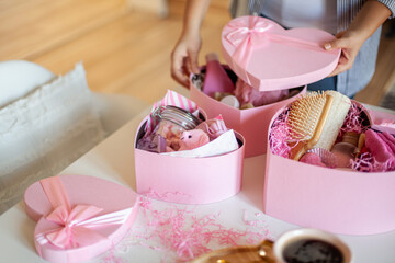 Woman hands holding pink colored heart shaped gift boxes of bath and body products for bridesmaids.