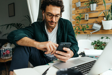 Man with laptop and smartphone working remotely from home, making video call on mobile phone....