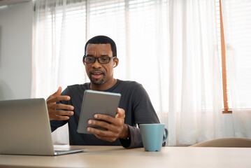 African-American man having video chat with digital tablet and laptop at home