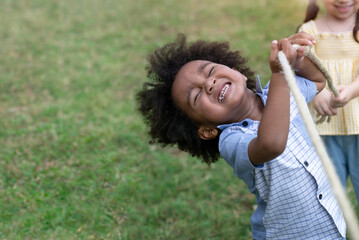 Obraz premium White and dark skinned kids have fun playing tugs at the park, group of happy multiethnic school kids, selective focus