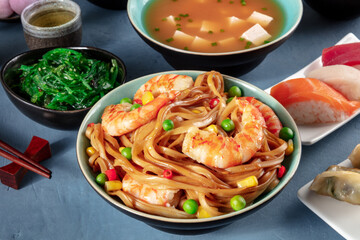 Japanese dinner. Stir-fried noodles with shrimps, miso soup, nigiri, wakame, green tea on a blue background