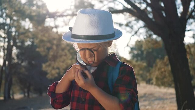 Travel, adventure concept. young naturalist kid is studying nature of forest with magnifying glasses. little girl looks through magnifying glass. kid travels through forest.kid dreams of an adventure.