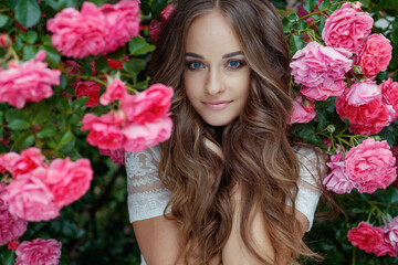 Obraz na płótnie Canvas Beautiful young woman with long hair posing near roses in the garden. Portrait of a woman with flowers. High quality photo.