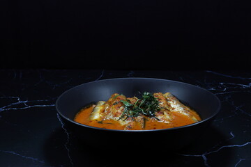 Spicy curry soup of Sheatfish (River fish) topping with cutting Kaffir lime leaves serving on the plate.