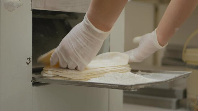 the baker's hands in gloves fold the blanks of dough cakes, rolled by a special machine. Production of the national flatbread lavash. Close-up.