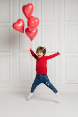 happy boy in jeans and sweater jumps with red balloons on white background with space for text