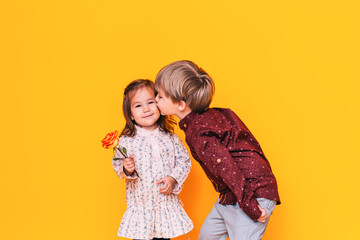 A boy in a shirt kisses a girl in a dress on the cheek against a yellow background. Valentine's Day. International Women's Day.