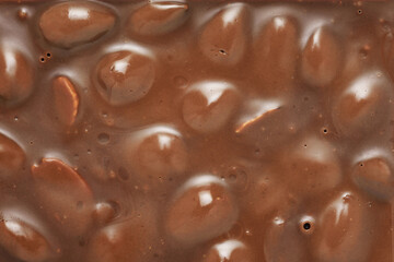 Brown milk chocolate bar with whole hazelnuts background.