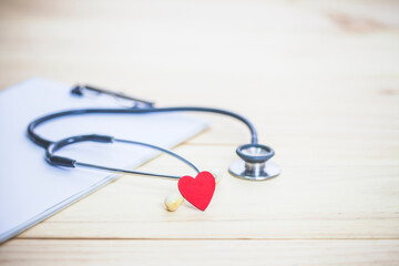 Red heart over Stethoscope on the table in doctor office, medical background with copy space.