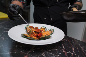 Chef puts mussels in pink sauce with white wine on a plate